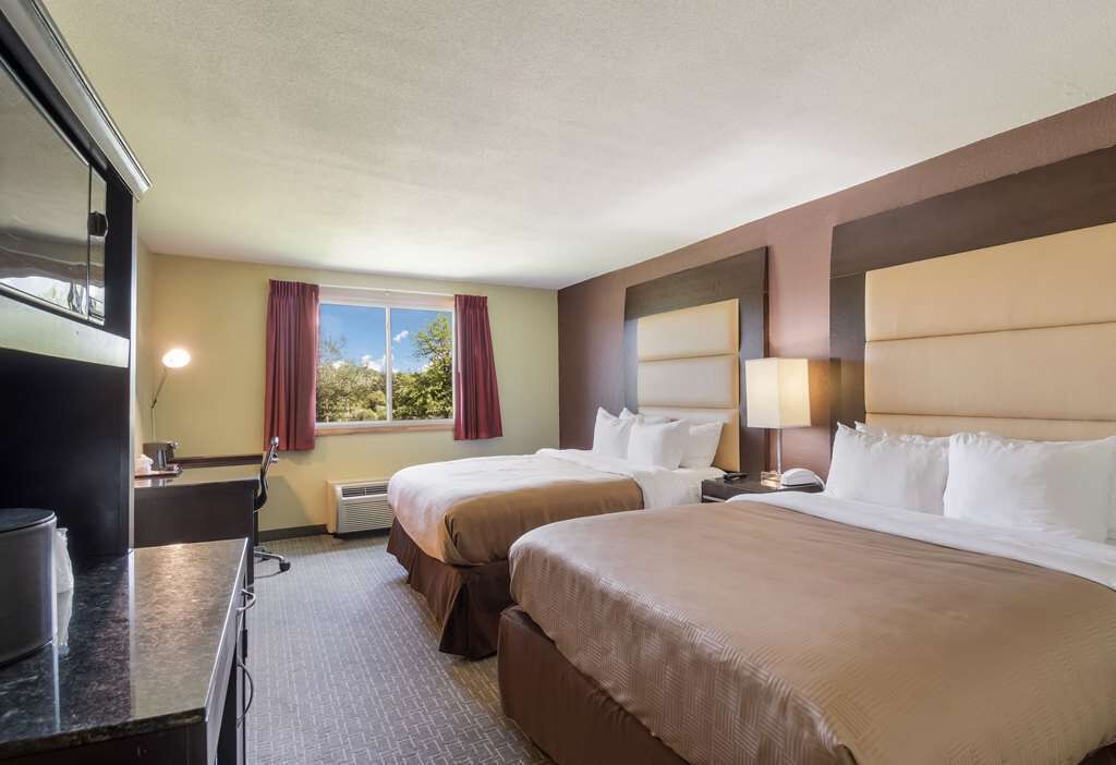 A hotel room with two beds, a desk, a television, and a window with curtains.