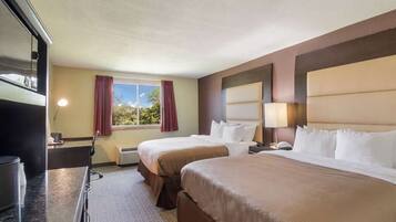 A hotel room with two beds, a desk, a television, and a window with curtains.