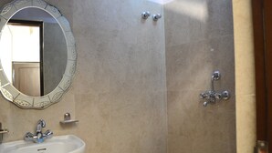 A bathroom with a white sink, a mirror with a decorative frame, and a shower with a handheld showerhead. - Hotel Abhinandan Inn Jaipur (Jaipur)