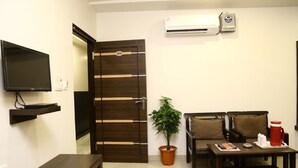 A compact hotel room with a dark wooden door, a flat-screen TV, a potted plant, a sofa with cushions, and a coffee table. - Hotel Abhinandan Inn Jaipur (Jaipur)