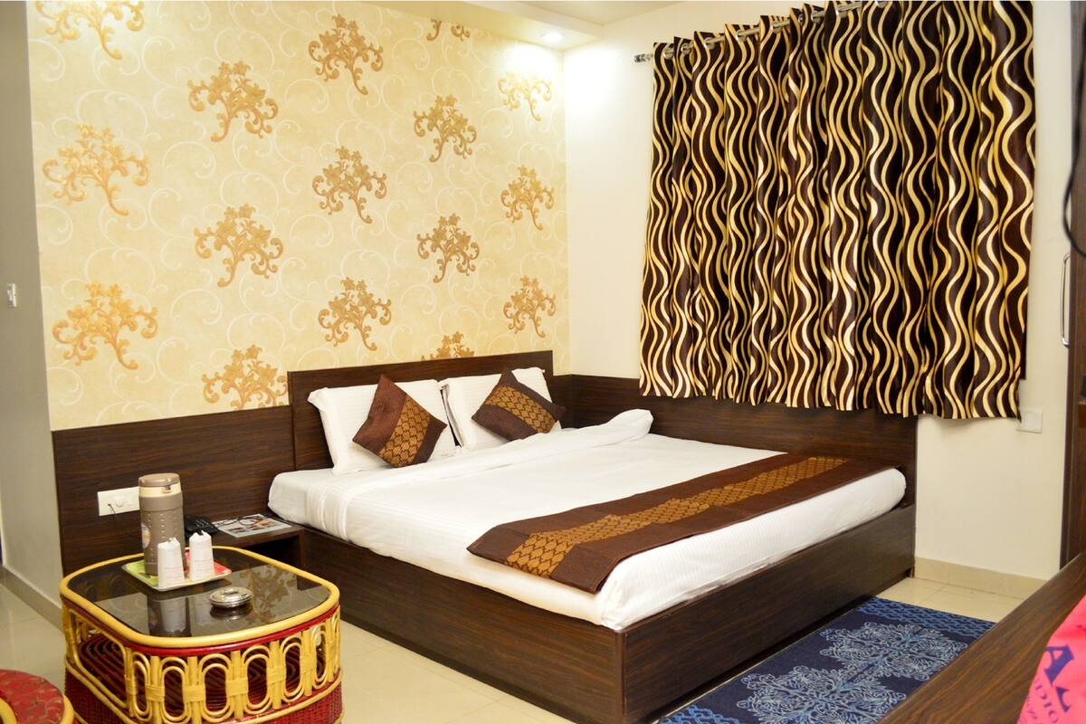 Une chambre d’hôtel avec un grand lit, une table de chevet, un mur décoré d’un motif et un rideau.