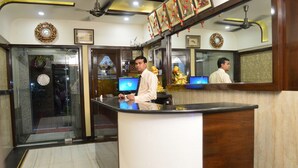 A reception area with a marble floor, a wooden reception desk, and a ceiling fan. - Hotel Abhinandan Inn Jaipur (Jaipur)