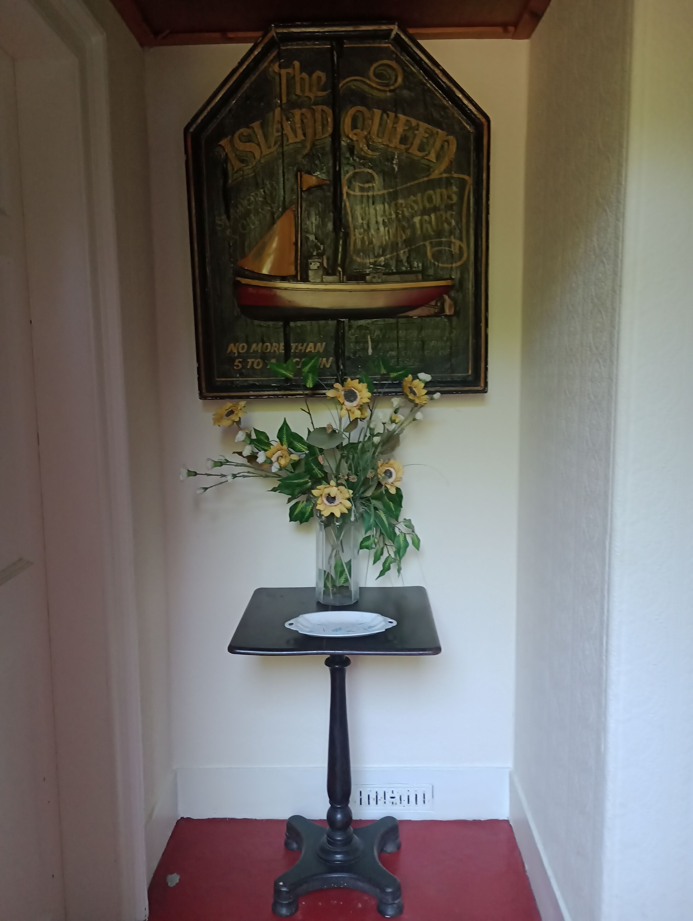 A vintage sign reading "The Island Queen" with a ship illustration, a vase with sunflowers, and a small table with a white dish.