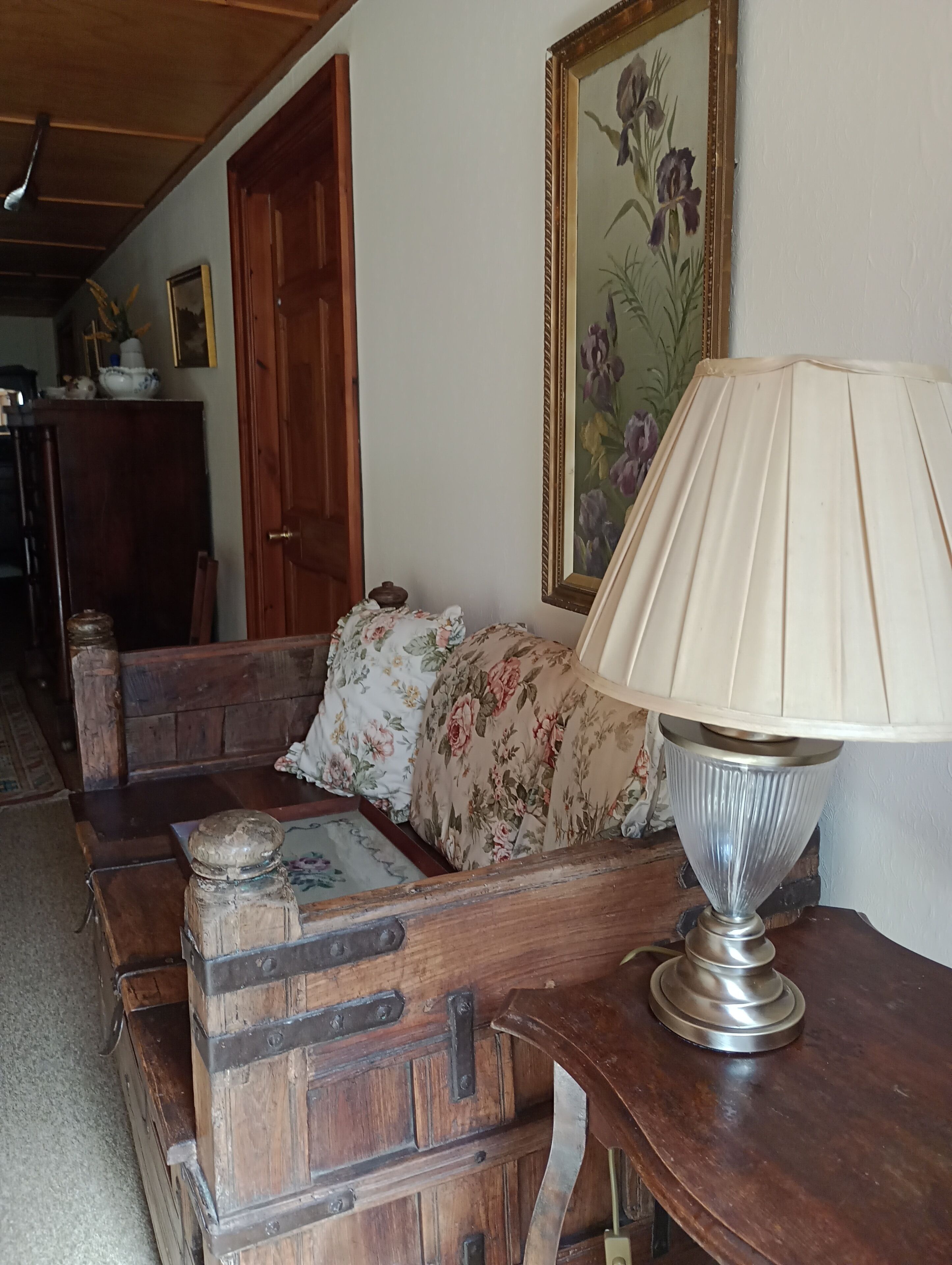 A wooden bench with a floral cushion, a metal lamp, and a painting of flowers on the wall.