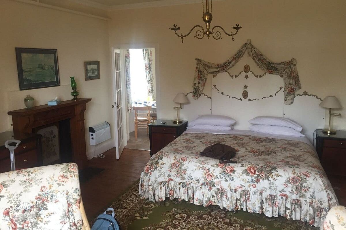 A bedroom with a floral bedspread, a wooden dresser, a desk, and a chair.
