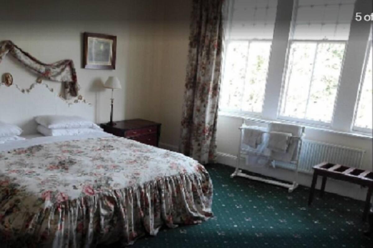A bedroom with a bed, a nightstand, a lamp, a window with curtains, and a radiator.
