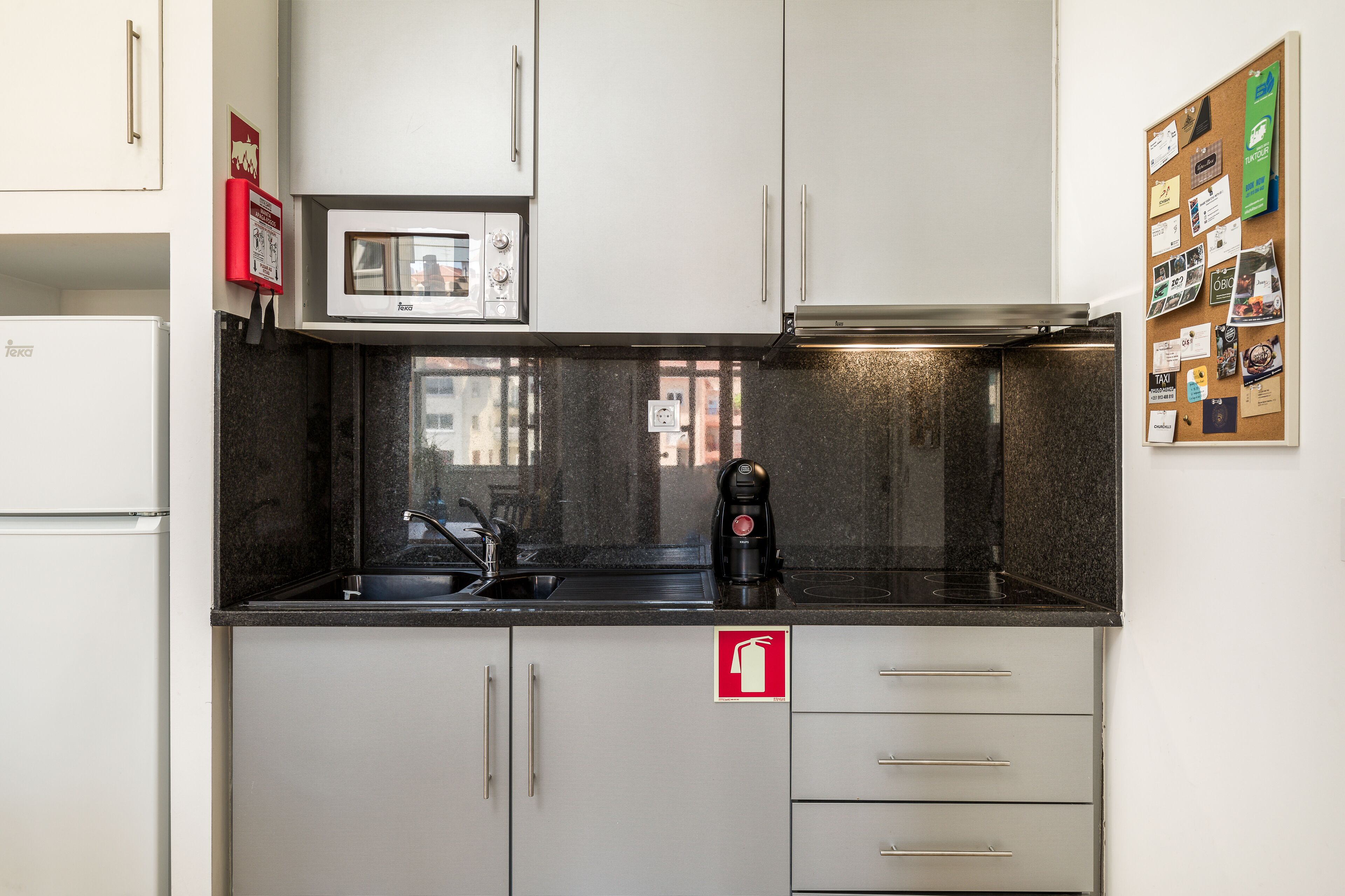 A compact kitchen with a microwave, coffee maker, and a fire exit sign.