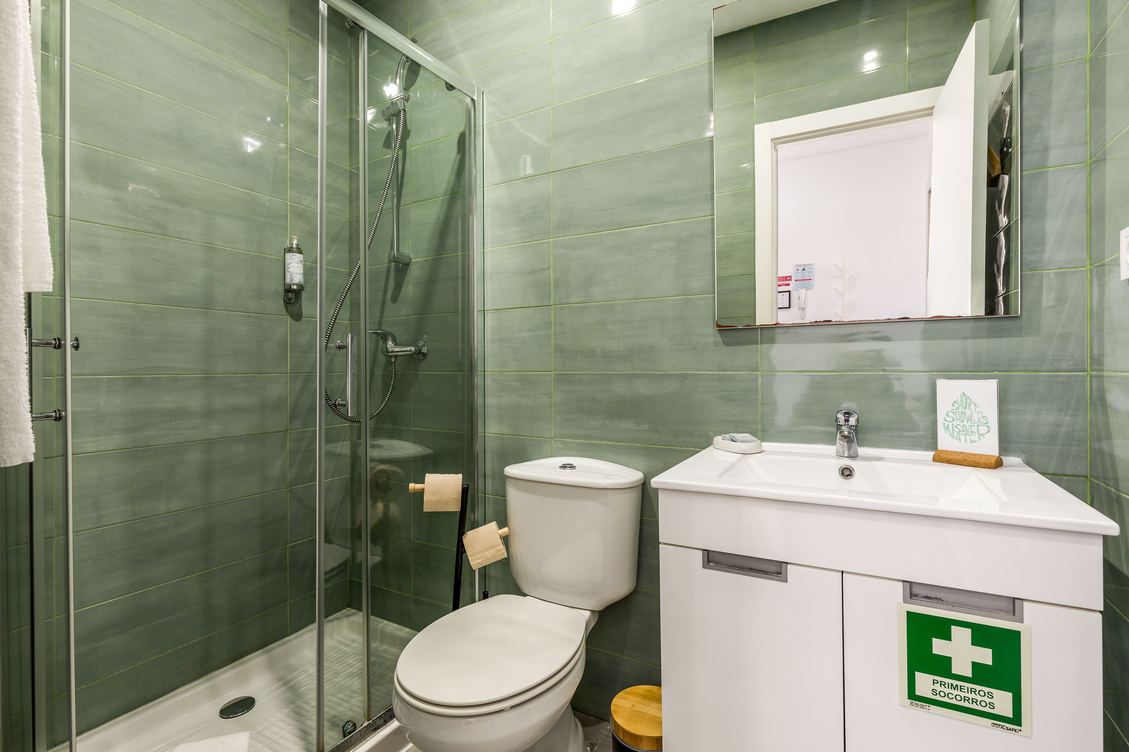 Een badkamer met een douche met glazen wand, een toilet en een wastafel met een bordje voor eerste hulp.