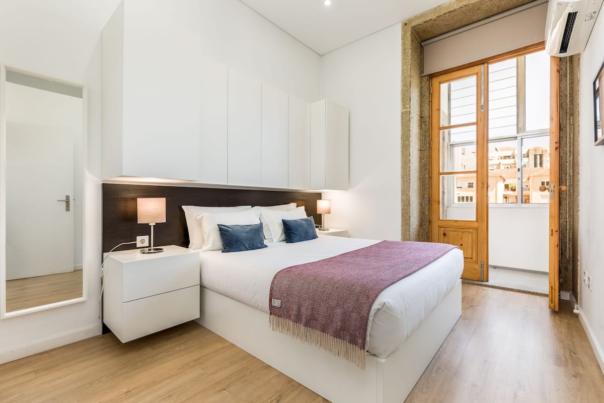 A modern bedroom with a large bed, bedside tables, and a view through a wooden door.