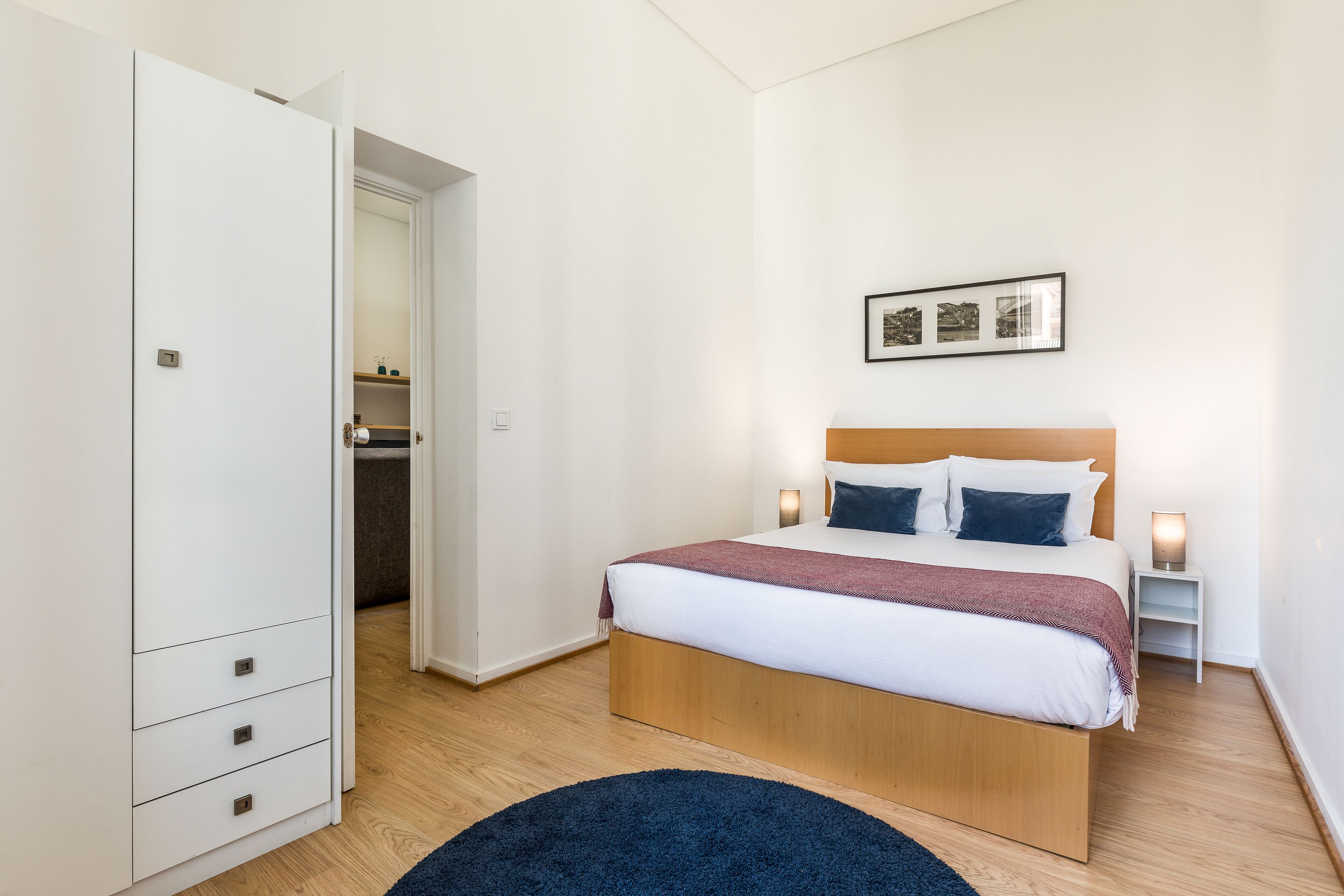 Een slaapkamer met een bed, nachtkastjes, een garderobe en een lijst met een afbeelding aan de muur.
