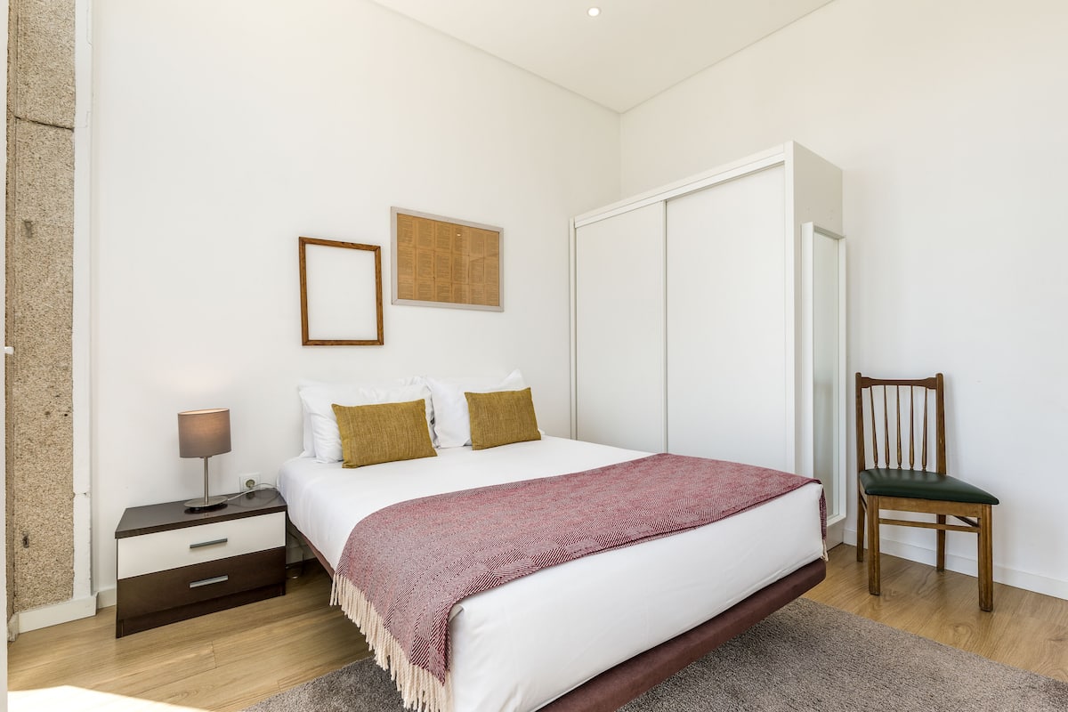 A bedroom with a bed, a nightstand, a chair, a wardrobe, and a framed picture on the wall.