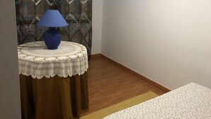 Una habitación con una mesa redonda, una lámpara azul, una cortina estampada, un televisor de pantalla plana en la pared y una alfombra con diseño en el suelo.