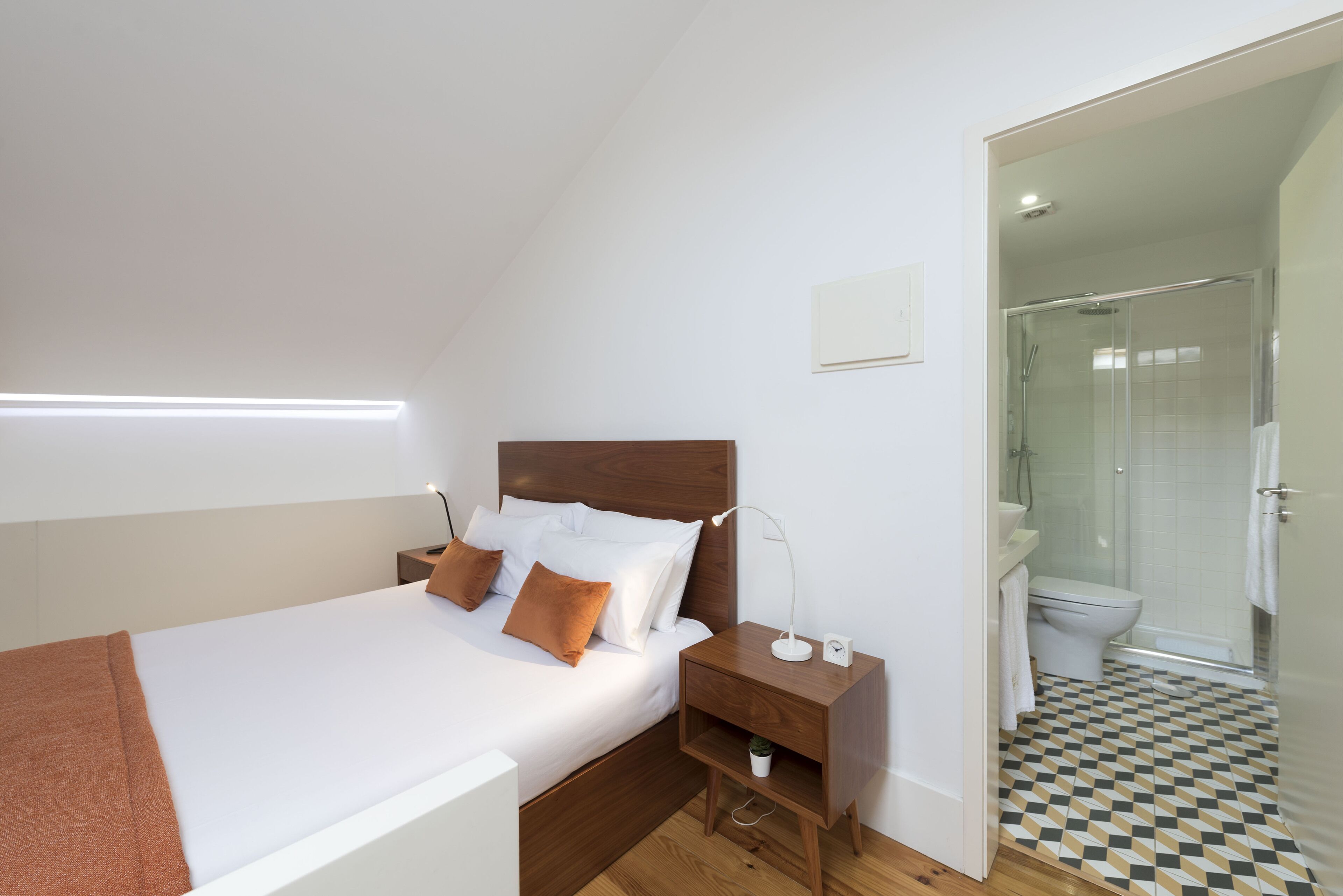 A modern bedroom with a wooden headboard, a white bed, and a nightstand with a lamp.