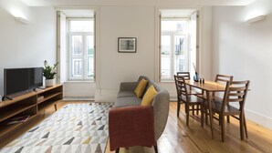 Een woonkamer met een bank, televisie, houten eettafel en stoelen.