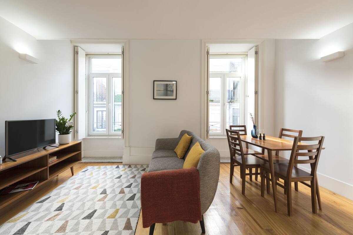 Een woonkamer met een bank, televisie, houten eettafel en stoelen.