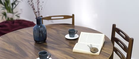 Una mesa redonda de madera con un florero azul, dos tazas y un libro abierto.