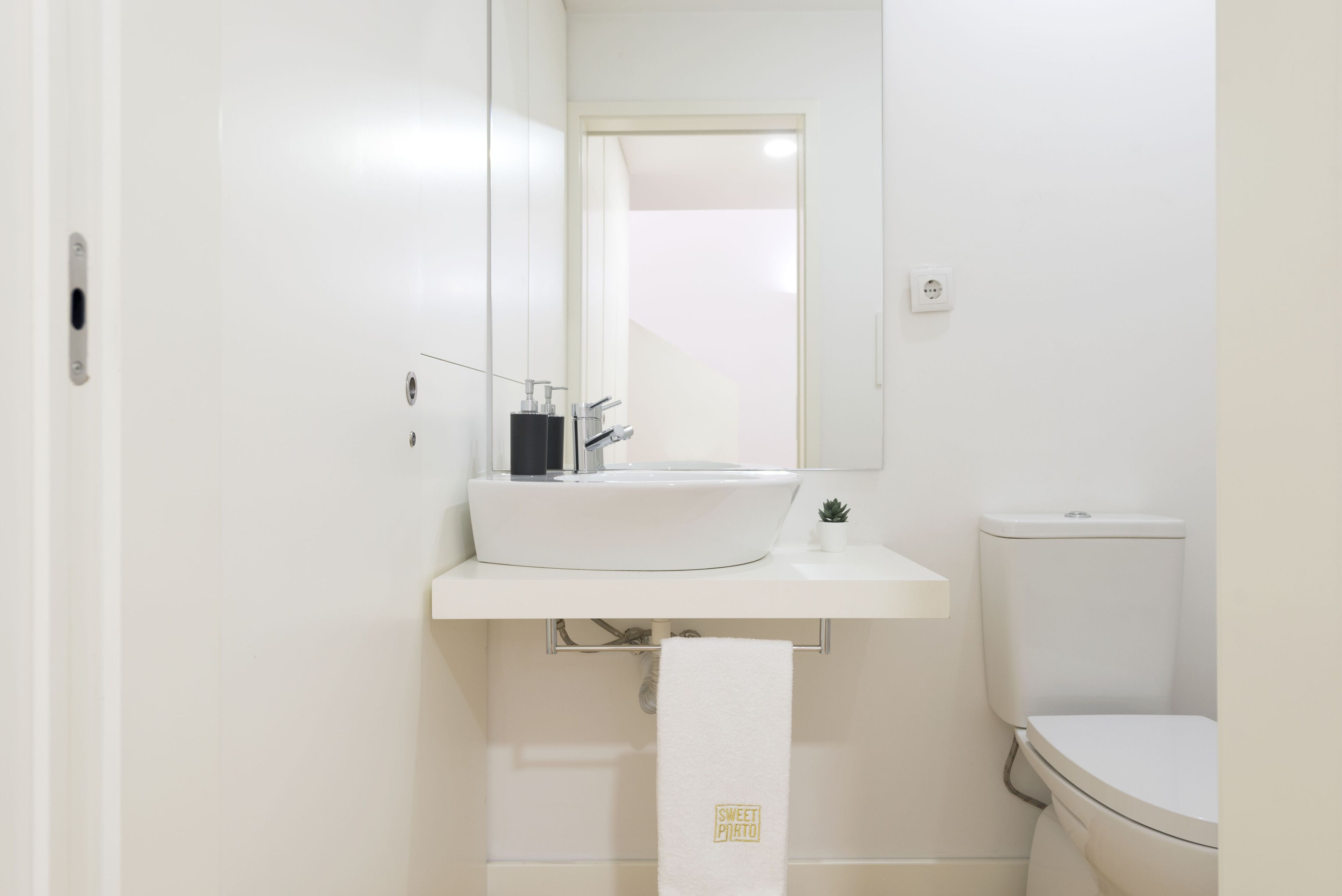 Ein kleines, sauberes Badezimmer mit weißem Waschbecken, Spiegel und Toilette.