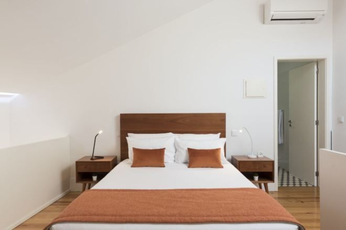 A bedroom with a wooden headboard, a white bedspread, two brown pillows, a brown throw blanket, and bedside lamps.