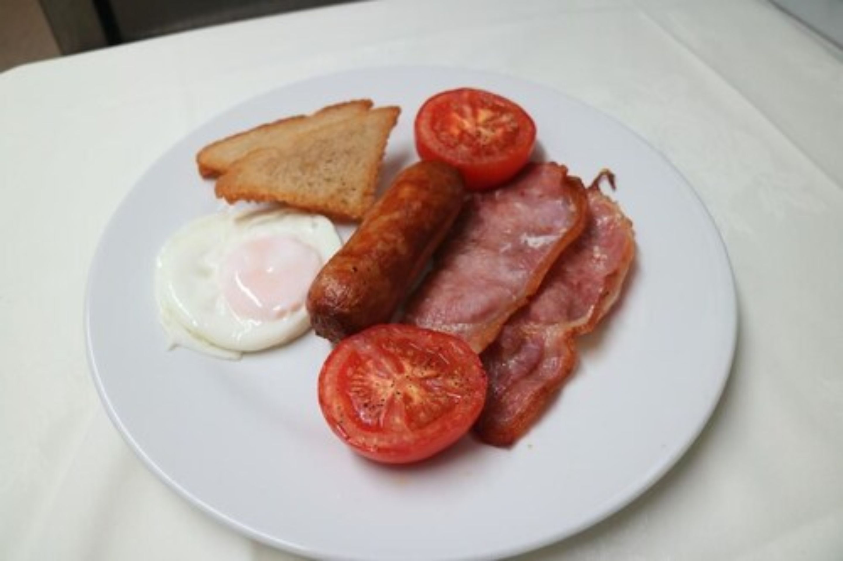 Un plato con tostadas, un huevo frito, salchichas, tocino y una rodaja de tomate.