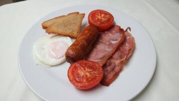 A plate with toast, a fried egg, sausages, bacon, and a tomato slice.