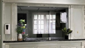 Uma área de recepção com balcão de mármore, uma placa acima e uma janela com cortinas translúcidas.