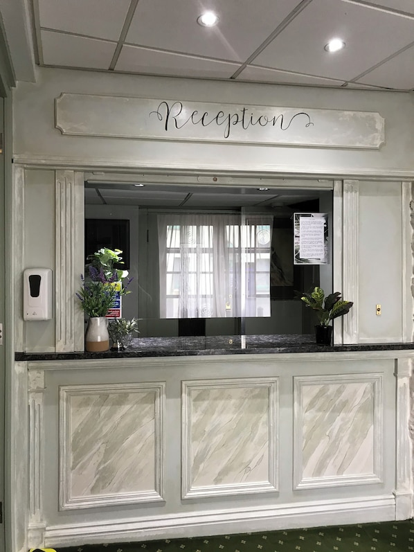 A reception area with a marble counter, a sign above it, and a window with sheer curtains. - Falcon Hotel (Carmarthen)