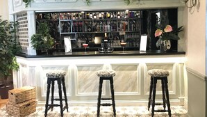 Uma área de bar com balcão branco, três banquetas e diversos frascos e copos.
