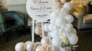 Arranjo decorativo de balões com uma placa que diz: "Bem-vindos ao nosso casamento Steve & Erica 14 de outubro de 2023".