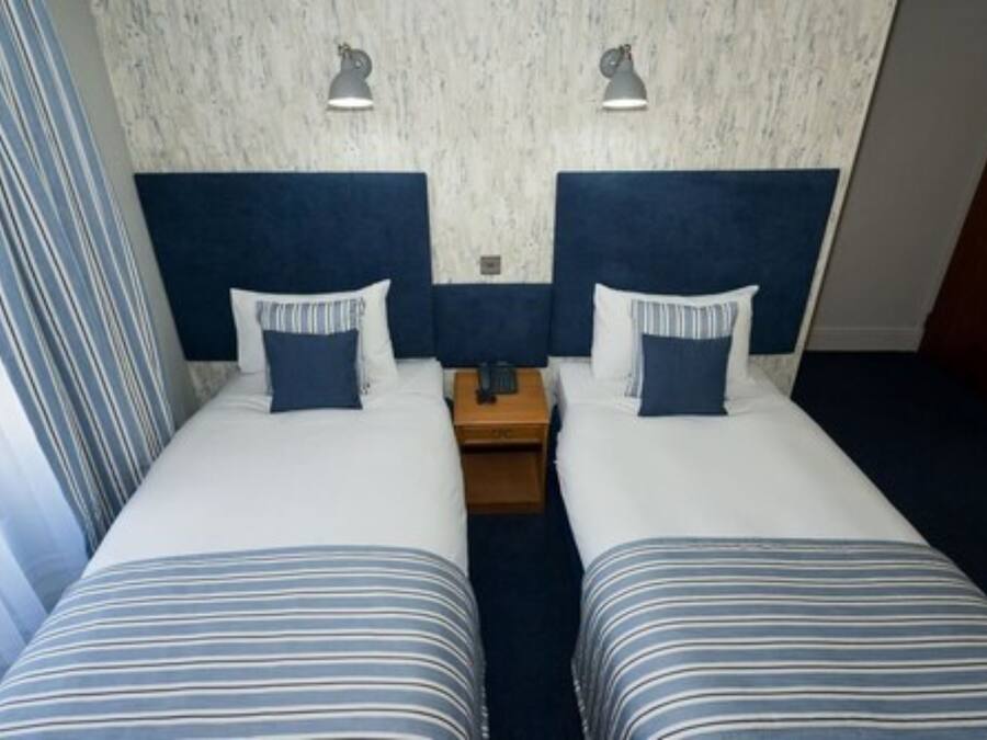 Een hotelkamer met twee bedden, elk voorzien van gestreept bedgoed en passende kussens, een houten nachtkastje en twee wandlampen.