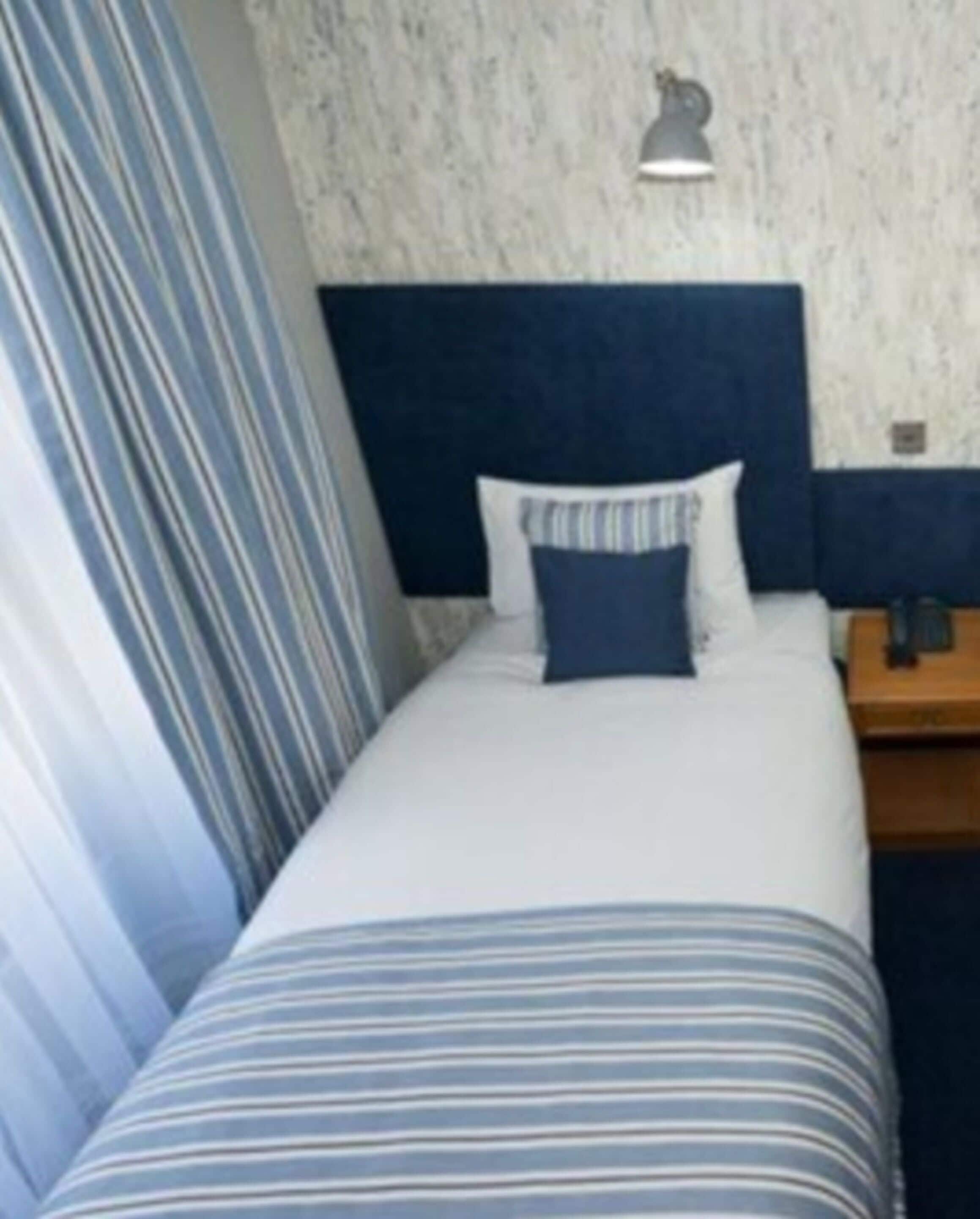 Una habitación de hotel con cama, mesita de noche, lámpara y cortina.