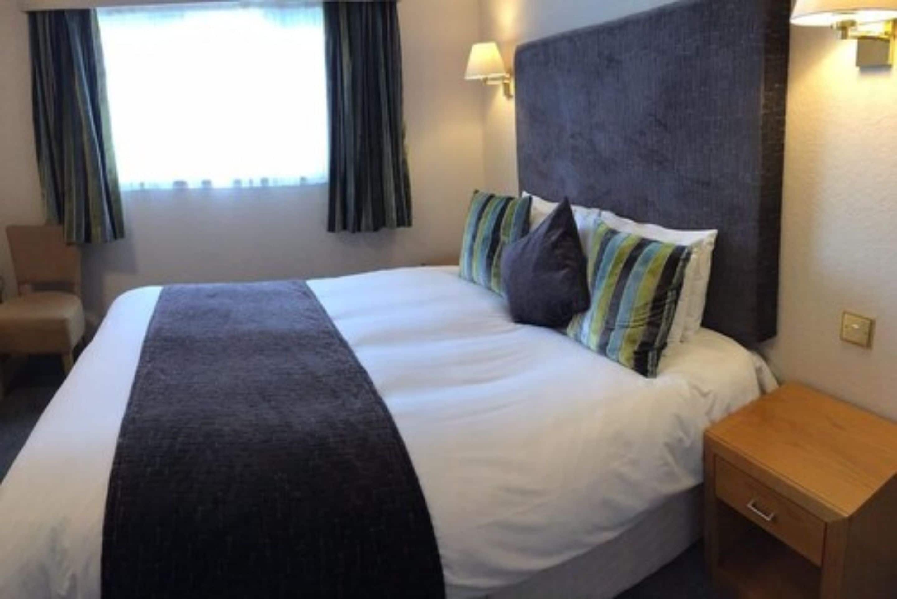 Una habitación de hotel con una cama grande, una mesita de noche, una silla y una ventana con cortinas.