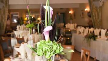 A dining area with tables set for service, featuring a centerpiece with flowers and a tall vase.