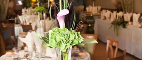A dining area with tables set for service, featuring a centerpiece with flowers and a tall vase.