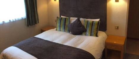 A neatly made bed with a dark headboard, two bedside tables with lamps, and a window with curtains.