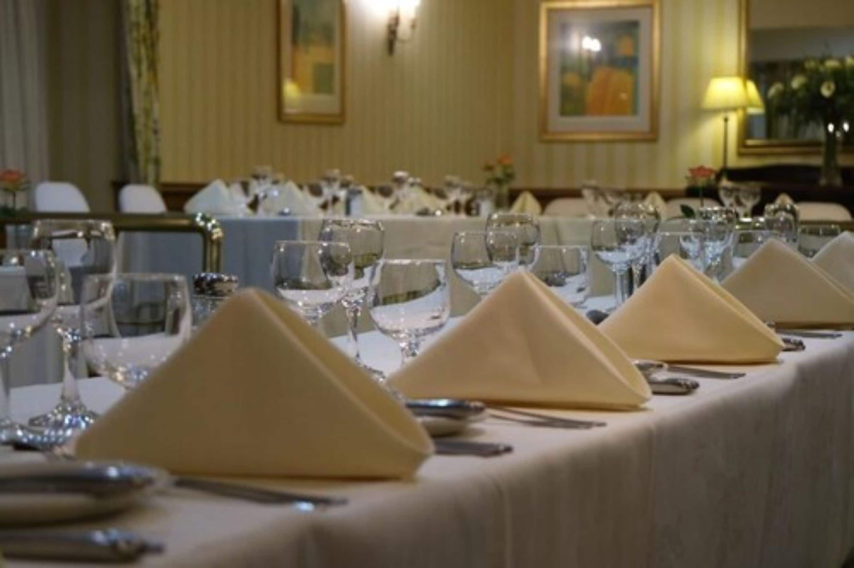 Uma sala de jantar formal com várias mesas preparadas para refeição, cada uma com guardanapo dobrado e copos de vinho.
