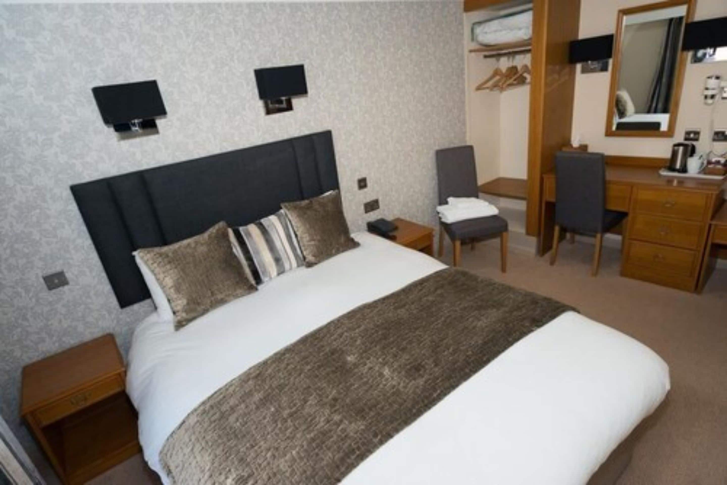 Ein ordentlich eingerichtetes Hotelzimmer mit Bett, Nachttischen, Schreibtisch, Stuhl und Kleiderschrank.