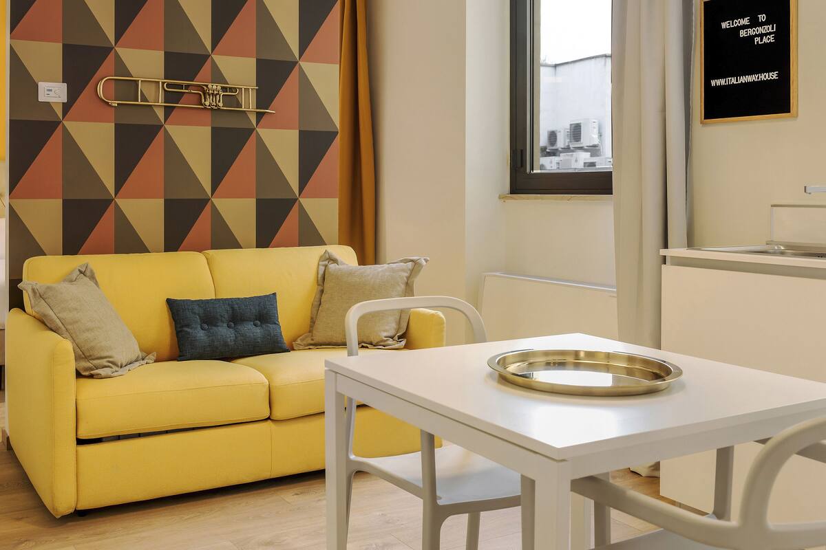 A yellow sofa with pillows, a white table, and a bed with a headboard.