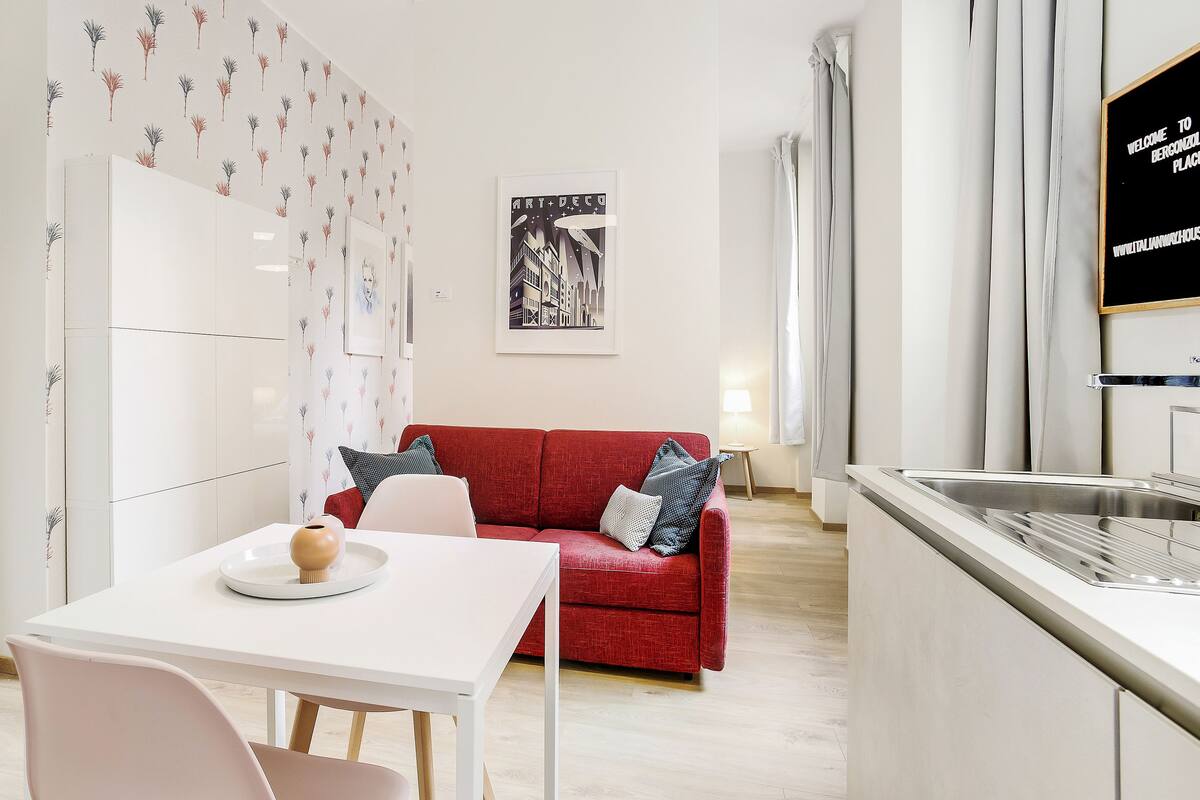 A modern kitchen with a red sofa, white dining table, and a poster on the wall.