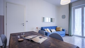 Una sala de estar moderna con una mesa de comedor de madera, un sofá azul y un ventanal grande.