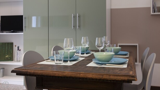 Una mesa de comedor dispuesta con platos azules, vasos transparentes y un tablero de madera.