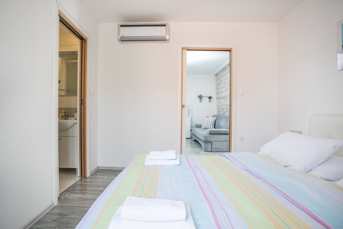 A hotel room with a bed, a bathroom, and a view of the hallway.