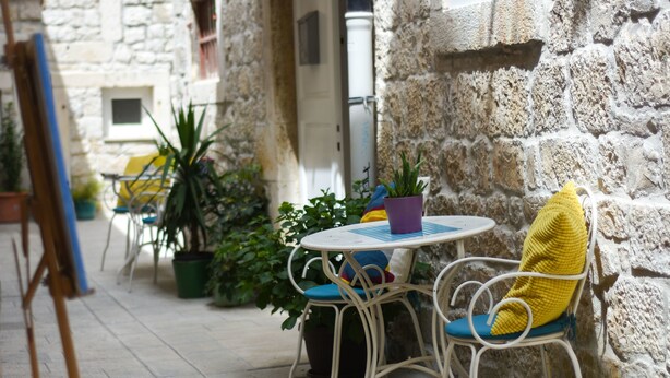 A stone-walled outdoor seating area with a round table and chairs, surrounded by potted plants. - Tragos Lemon Tree (Trogir)