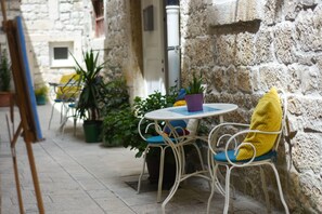 A stone-walled outdoor seating area with a round table and chairs, surrounded by potted plants. - Tragos Lemon Tree (Trogir)