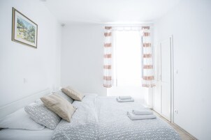 Quarto com cama, almofadas, um quadro na parede e janela com cortinas.