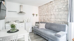 A modern kitchen with white cabinets, a grey sofa, and a stone wall. - Tragos Lemon Tree (Trogir)