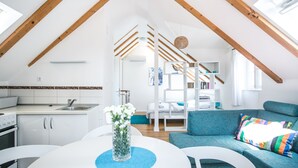 A modern loft apartment with exposed wooden beams, a kitchen with white cabinets, a dining area with a white table, and a blue sofa with colorful cushions. - Tragos Lemon Tree (Trogir)