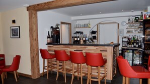 Un espace bar avec des tabourets en bois et un comptoir, équipé d’une machine à café et de diverses bouteilles.