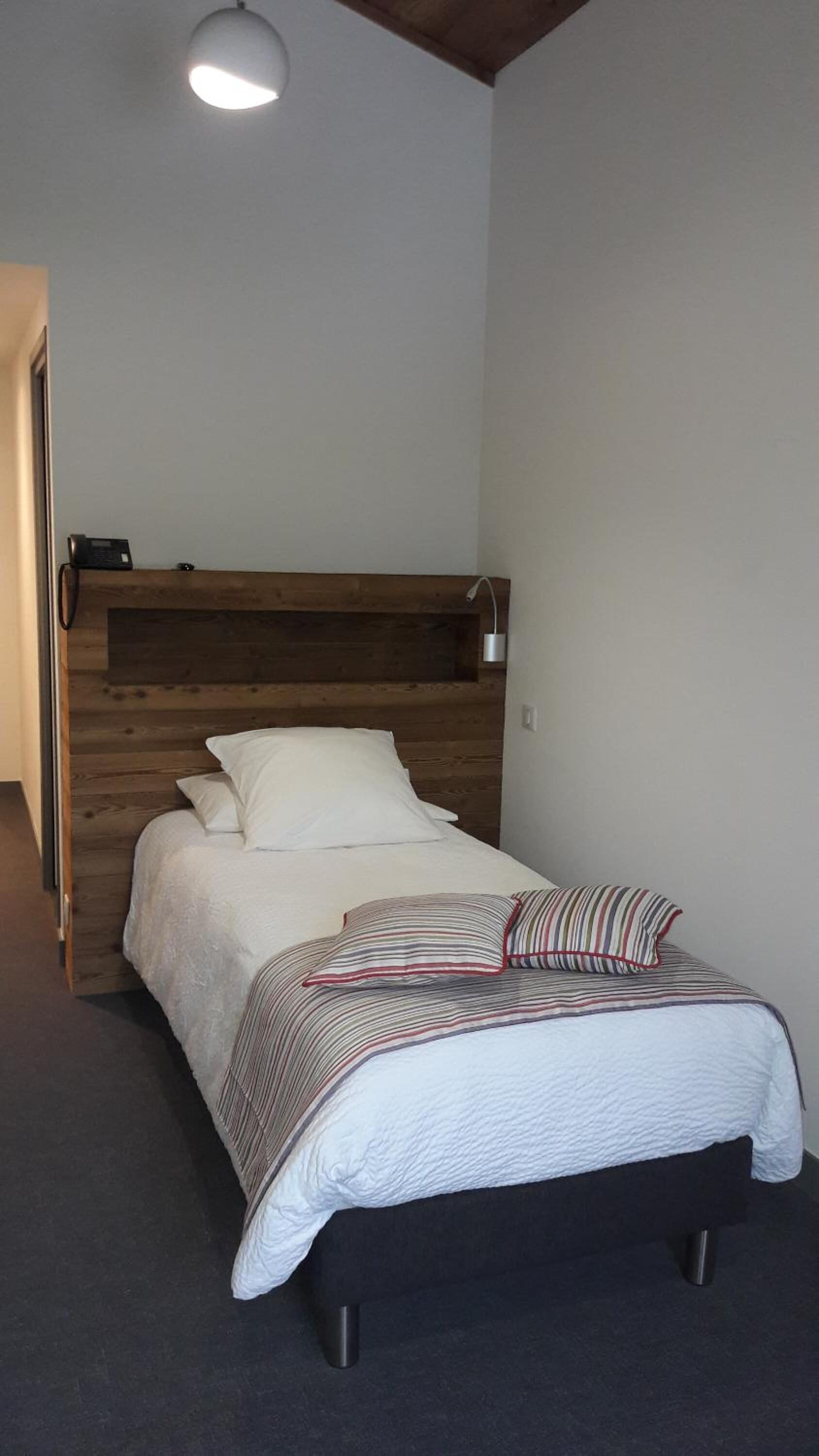 A bedroom with a wooden headboard, a bed with white bedding and striped pillows, a bedside lamp, and a door to the left.