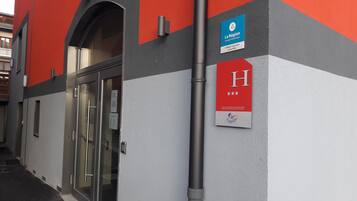 Entrada de un hotel con puerta de cristal, un letrero que indica 'La Région' y una 'H' para 'Hotel', y una placa con el logo de 'France' y una clasificación por estrellas.