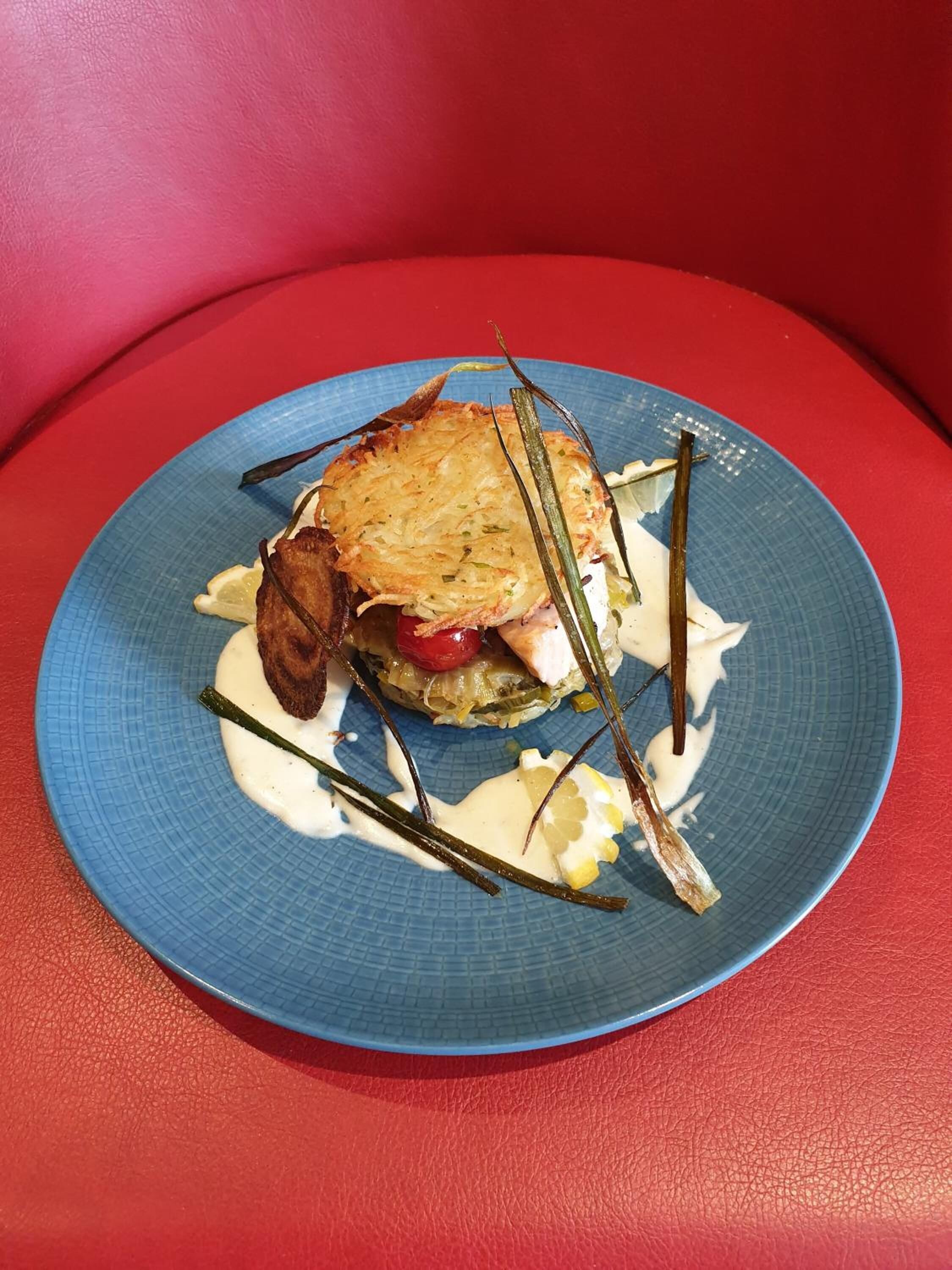 A plate with a sandwich, some vegetables, and a creamy sauce on a blue plate.